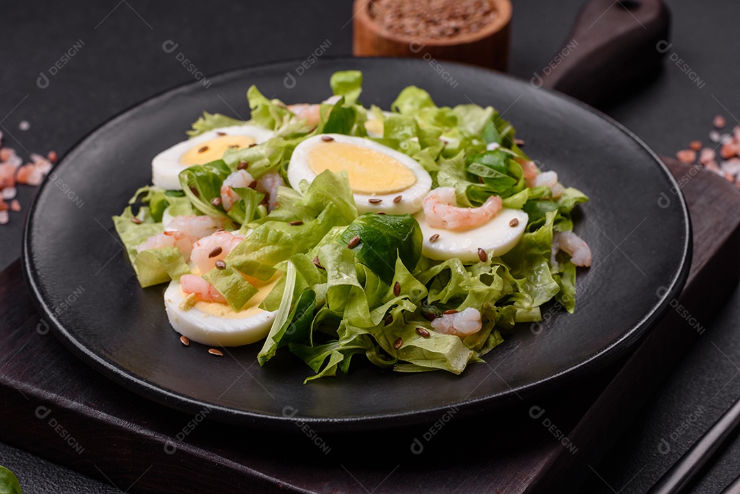 Deliciosa salada fresca e saudável com camarão, ovo, alface e sementes de linho em uma placa de cerâmica preta sobre um fundo de concreto