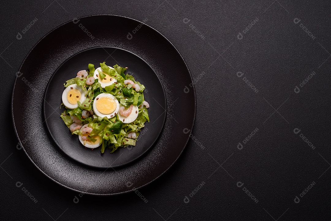 Deliciosa salada fresca e saudável com camarão, ovo, alface e sementes de linho em uma placa de cerâmica preta sobre um fundo de concreto