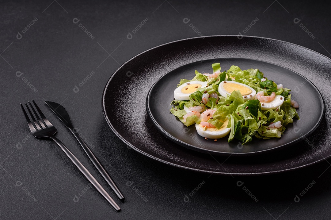 Deliciosa salada fresca e saudável com camarão, ovo, alface e sementes de linho em uma placa de cerâmica preta sobre um fundo de concreto