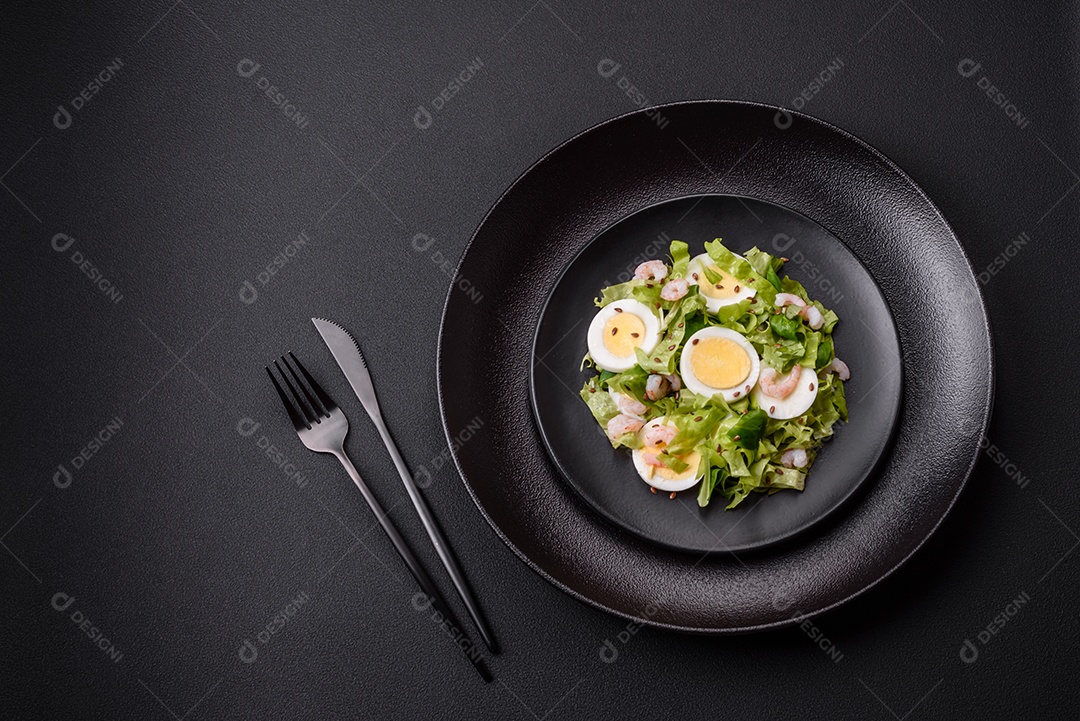 Deliciosa salada fresca e saudável com camarão, ovo, alface e sementes de linho em uma placa de cerâmica preta sobre um fundo de concreto