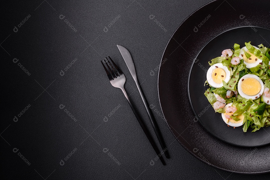 Deliciosa salada fresca e saudável com camarão, ovo, alface e sementes de linho em uma placa de cerâmica preta sobre um fundo de concreto