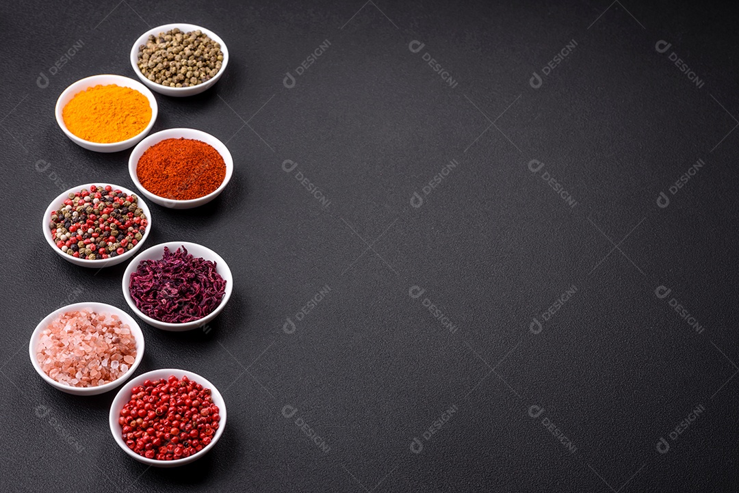 Composição composta por uma variação de diversos tipos de especiarias em tigelas de cerâmica branca sobre fundo de concreto texturizado