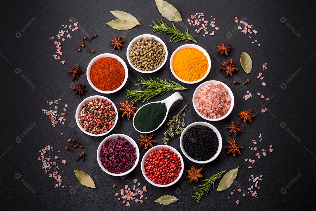 Composição composta por uma variação de diversos tipos de especiarias em tigelas de cerâmica branca sobre fundo de concreto texturizado