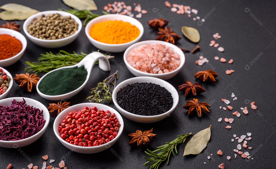 Composição composta por uma variação de diversos tipos de especiarias em tigelas de cerâmica branca sobre fundo de concreto texturizado