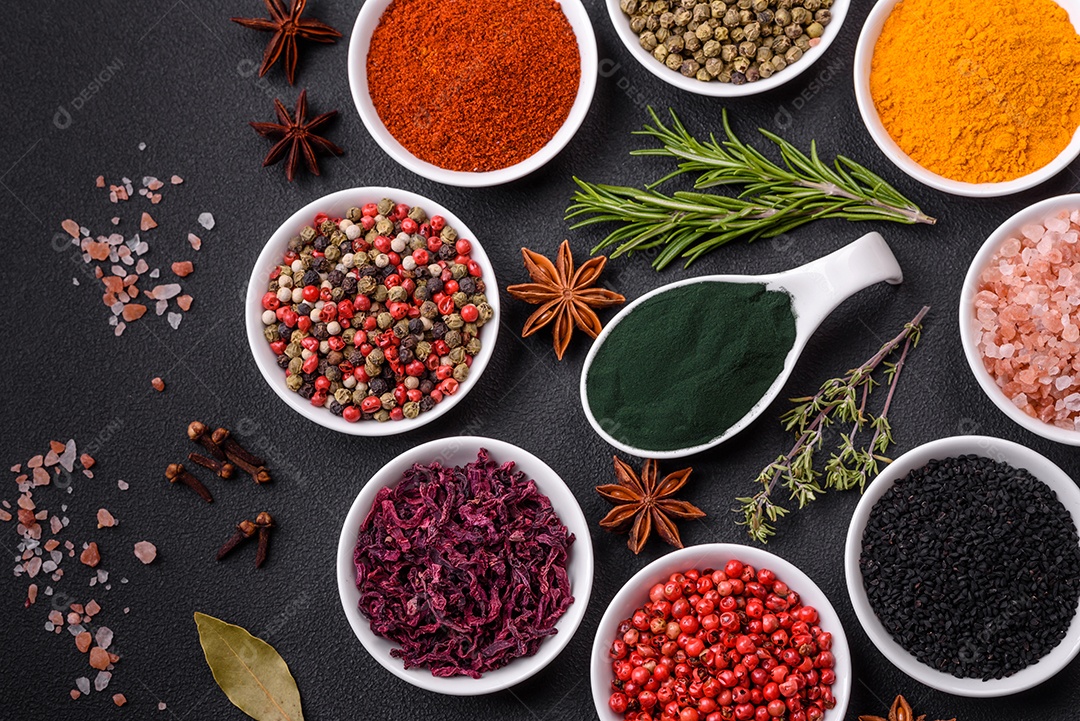 Composição composta por uma variação de diversos tipos de especiarias em tigelas de cerâmica branca sobre fundo de concreto texturizado