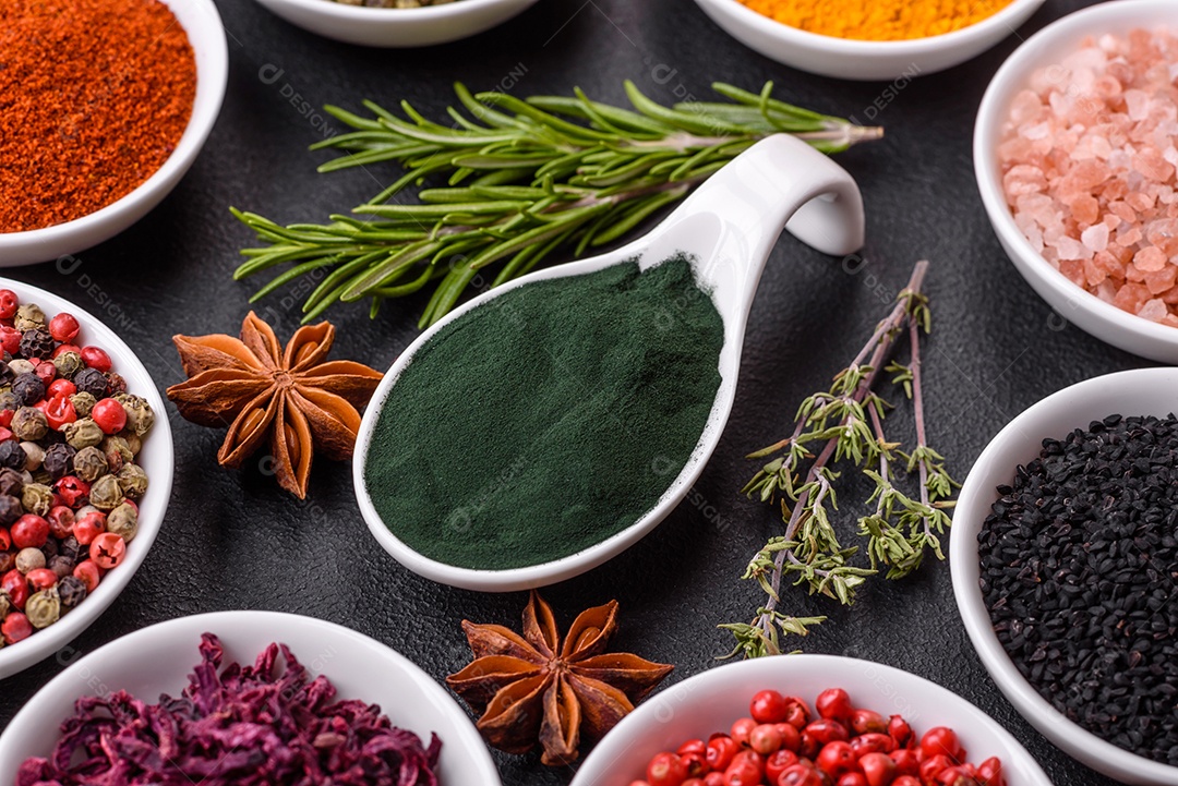 Composição composta por uma variação de diversos tipos de especiarias em tigelas de cerâmica branca sobre fundo de concreto texturizado