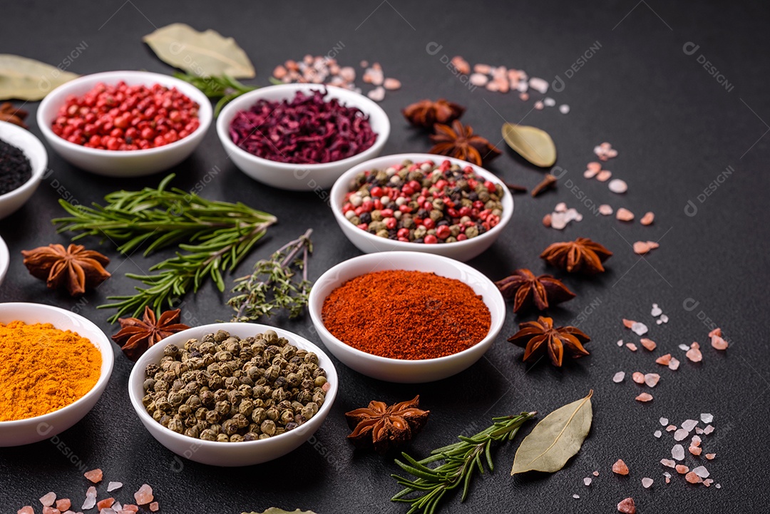 Composição composta por uma variação de diversos tipos de especiarias em tigelas de cerâmica branca sobre fundo de concreto texturizado