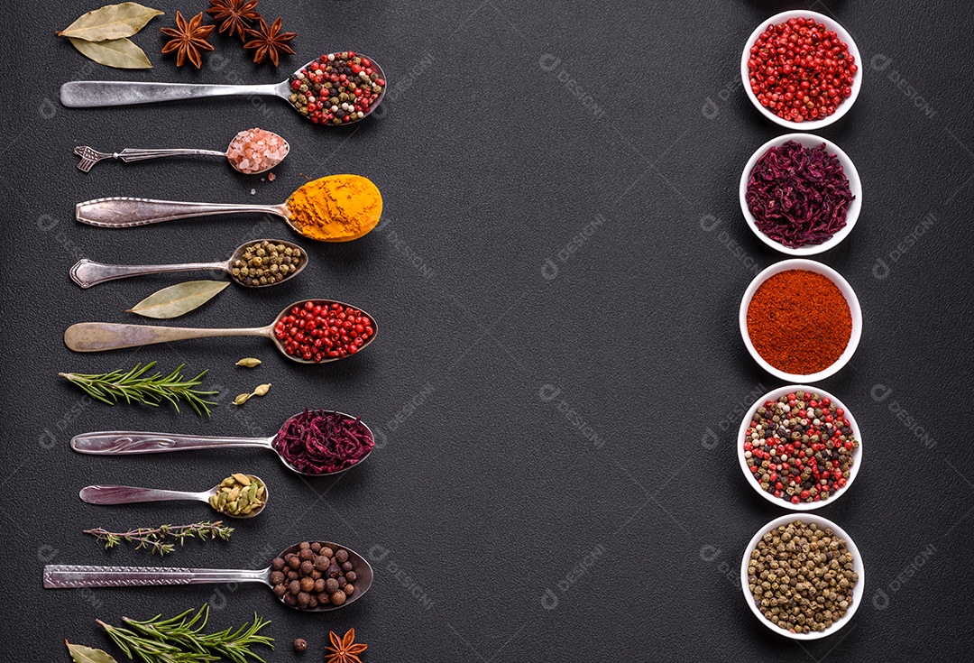 Composição composta por variações de especiarias em tigelas brancas e colheres de metal sobre fundo escuro de concreto