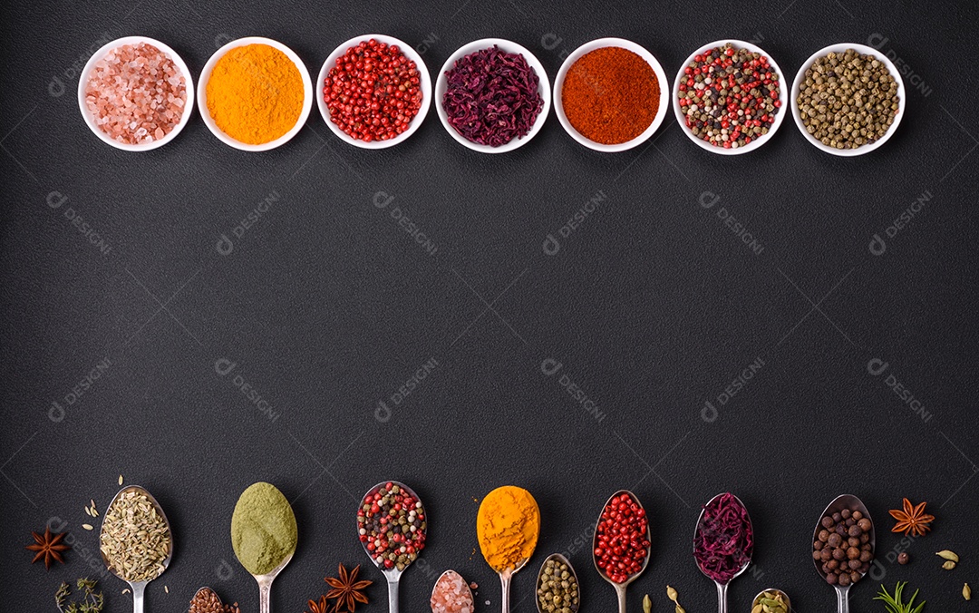 Composição composta por variações de especiarias em tigelas brancas e colheres de metal sobre fundo escuro de concreto