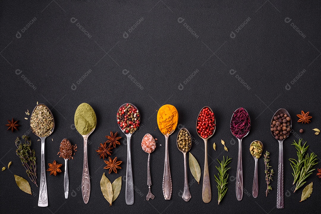 Composição composta por variações de especiarias em tigelas brancas e colheres de metal sobre fundo escuro de concreto