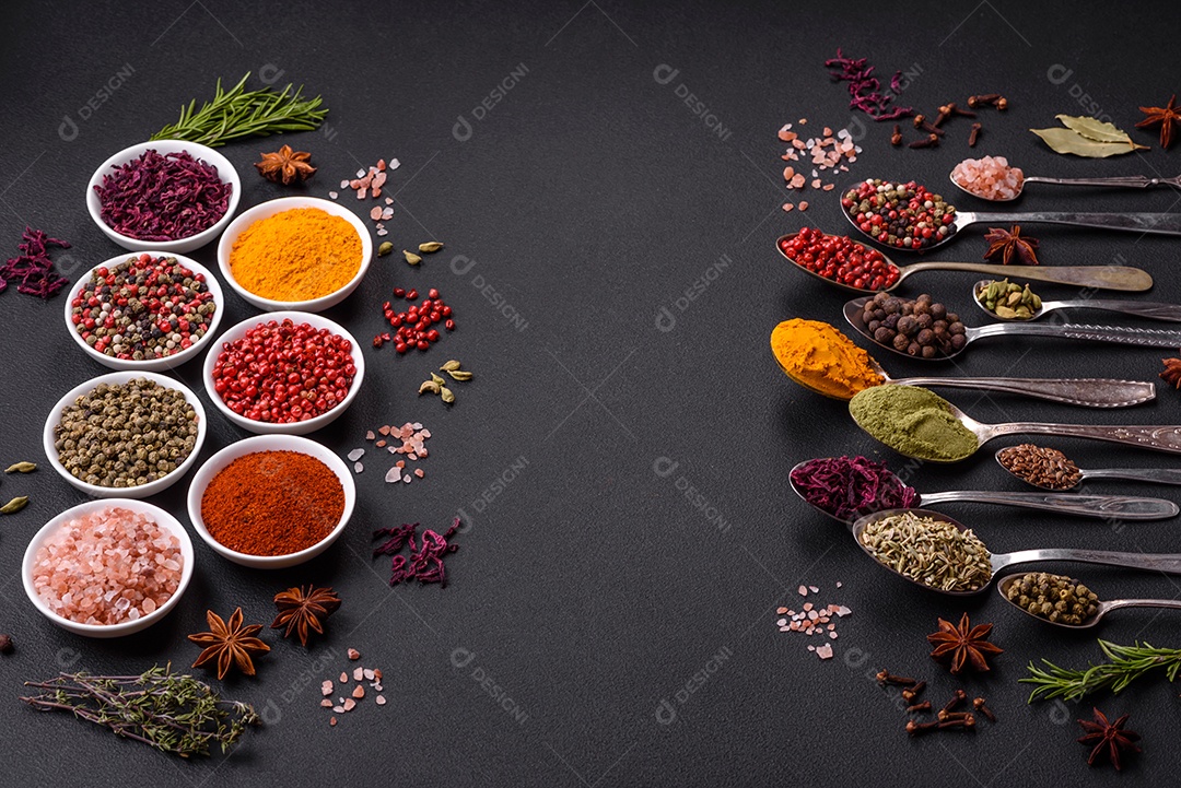 Composição composta por variações de especiarias em tigelas brancas e colheres de metal sobre fundo escuro de concreto