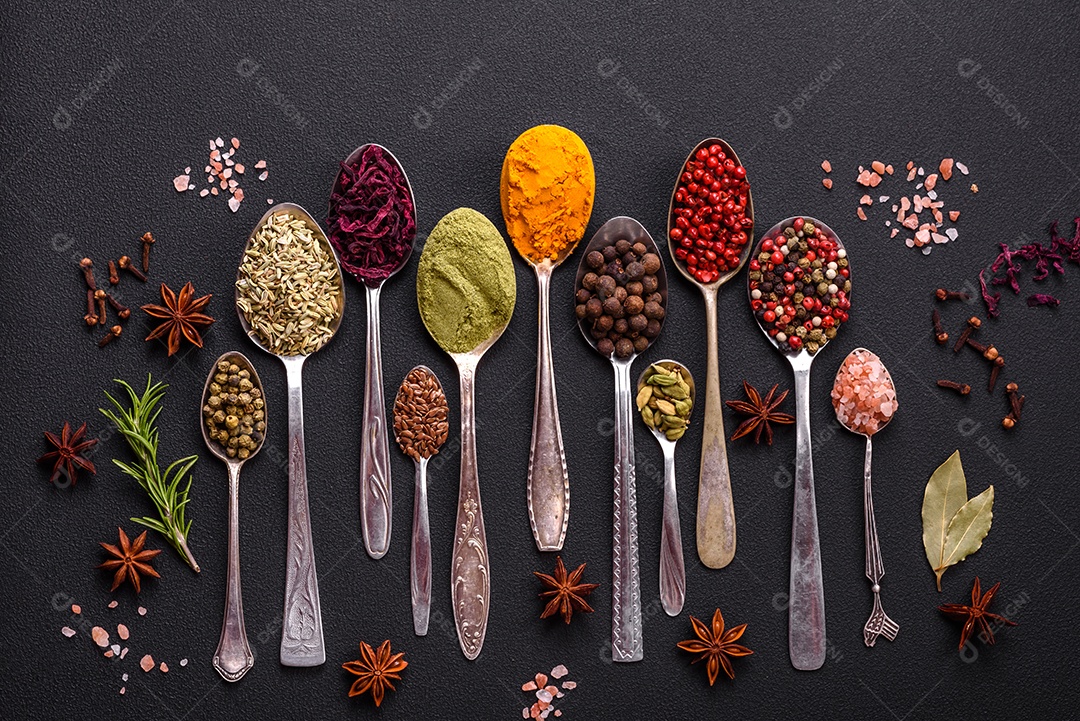 Composição composta por variações de especiarias em tigelas brancas e colheres de metal sobre fundo escuro de concreto