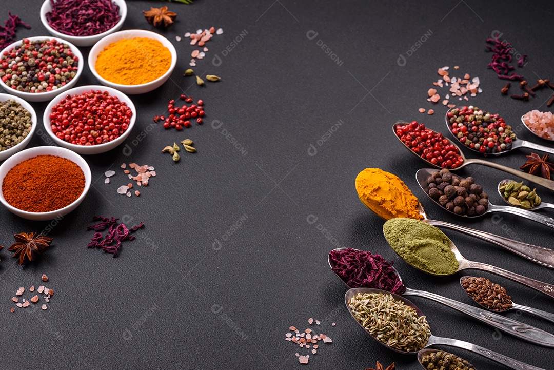 Composição composta por variações de especiarias em tigelas brancas e colheres de metal sobre fundo escuro de concreto