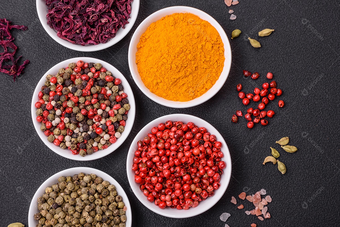 Composição composta por variações de especiarias em tigelas brancas e colheres de metal sobre fundo escuro de concreto