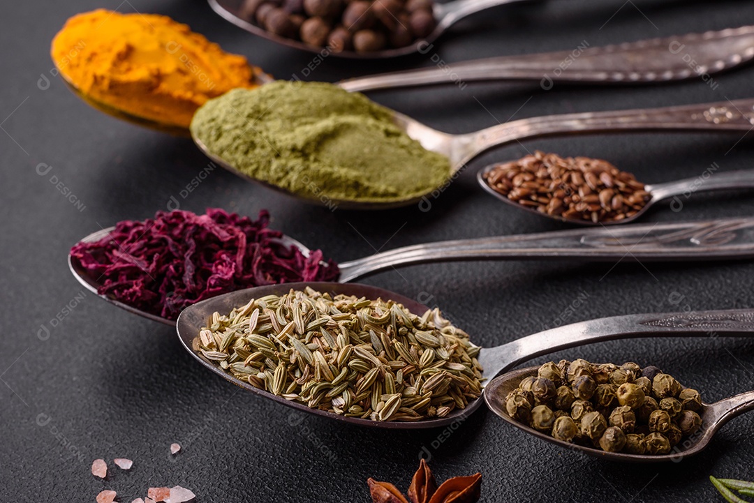 Composição composta por variações de especiarias em tigelas brancas e colheres de metal sobre fundo escuro de concreto