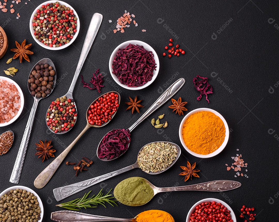 Composição composta por variações de especiarias em tigelas brancas e colheres de metal sobre fundo escuro de concreto