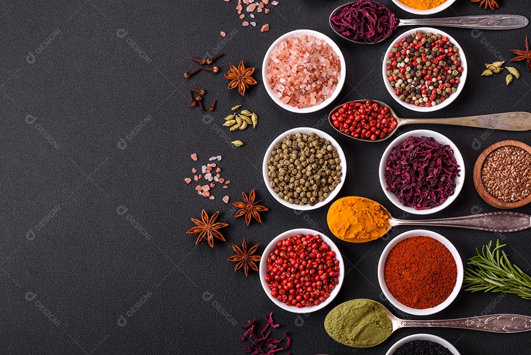 Composição composta por variações de especiarias em tigelas brancas e colheres de metal sobre fundo escuro de concreto