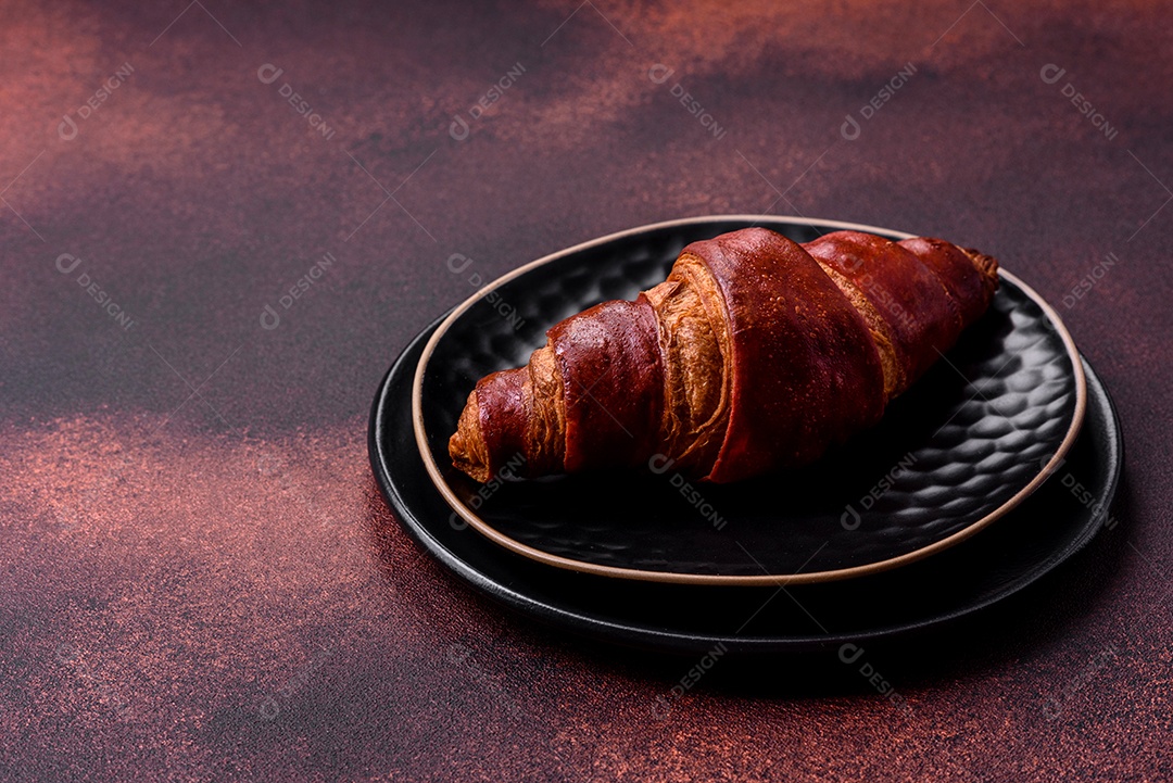Delicioso croissant crocante com chocolate em uma placa de cerâmica preta sobre um fundo escuro de concreto