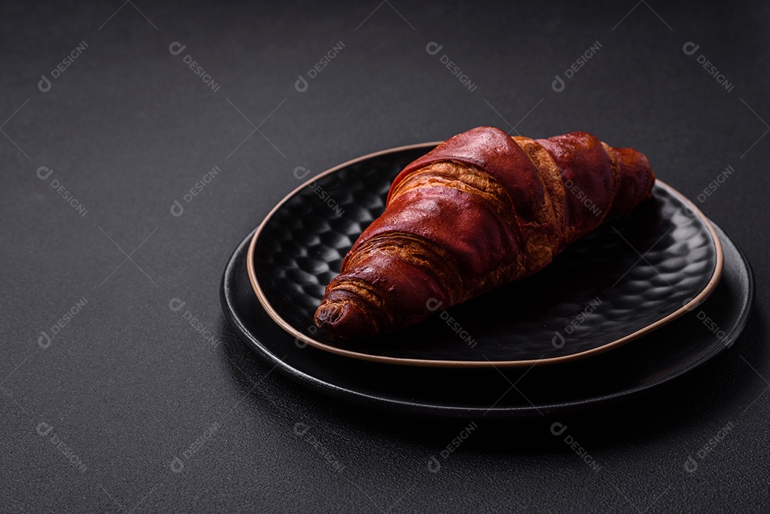 Delicioso croissant crocante com chocolate em uma placa de cerâmica preta sobre um fundo escuro de concreto