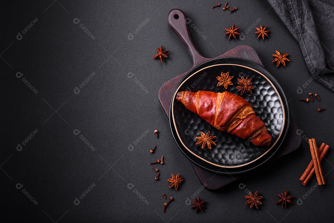 Delicioso croissant crocante com chocolate em uma placa de cerâmica preta sobre um fundo escuro de concreto