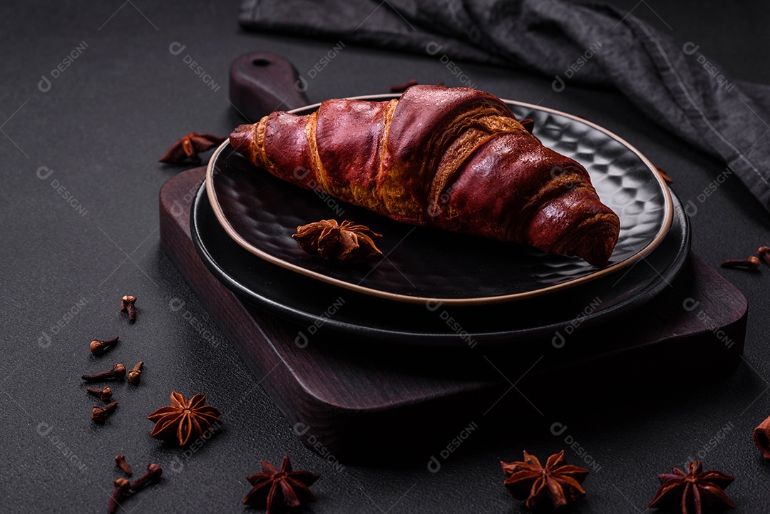 Delicioso croissant crocante com chocolate em uma placa de cerâmica preta sobre um fundo escuro de concreto