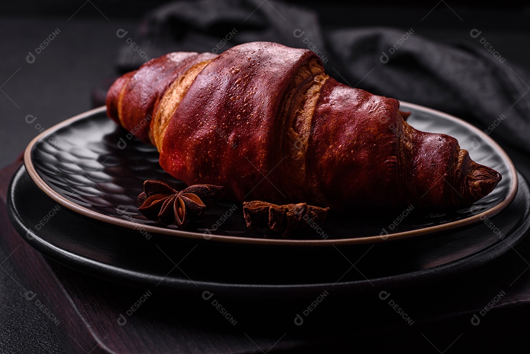 Delicioso croissant crocante com chocolate em uma placa de cerâmica preta sobre um fundo escuro de concreto