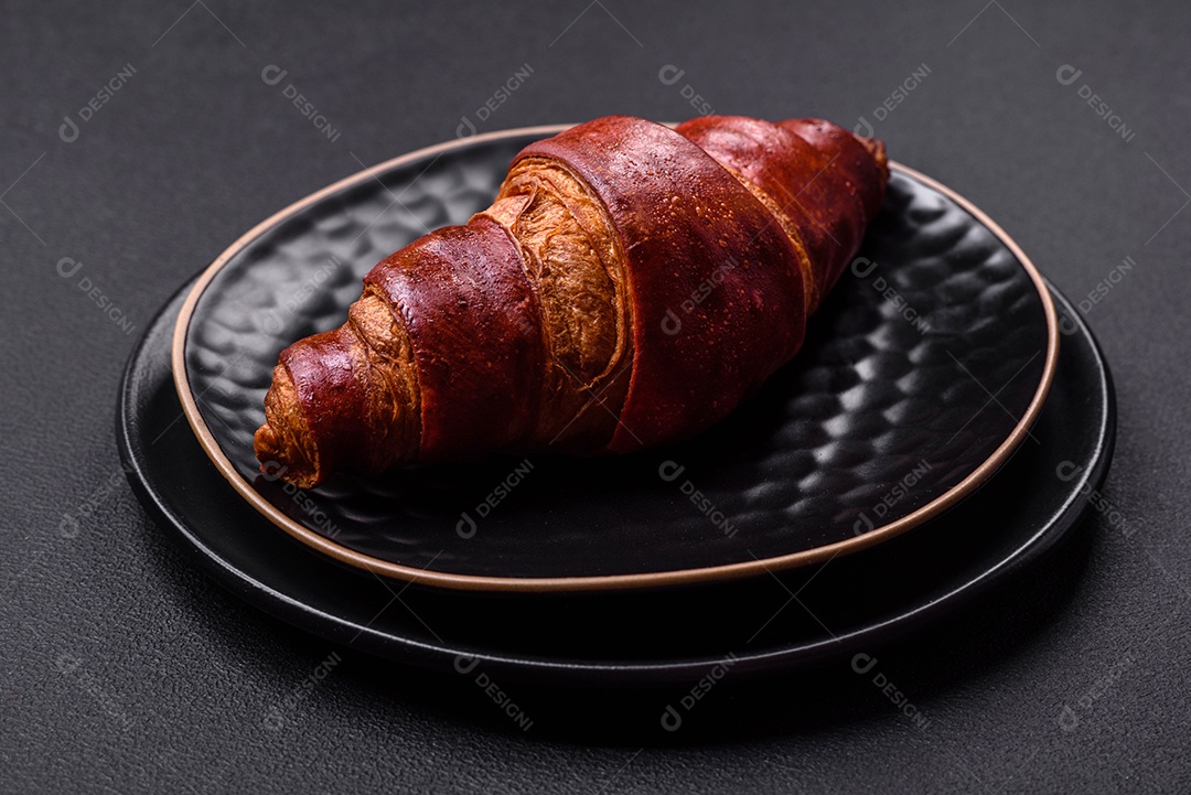 Delicioso croissant crocante com chocolate em uma placa de cerâmica preta sobre um fundo escuro de concreto