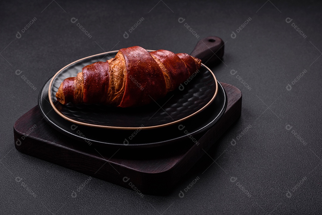 Delicioso croissant crocante com chocolate em uma placa de cerâmica preta sobre um fundo escuro de concreto