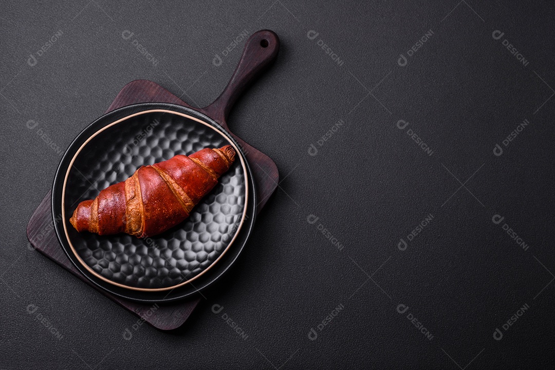 Delicioso croissant crocante com chocolate em uma placa de cerâmica preta sobre um fundo escuro de concreto