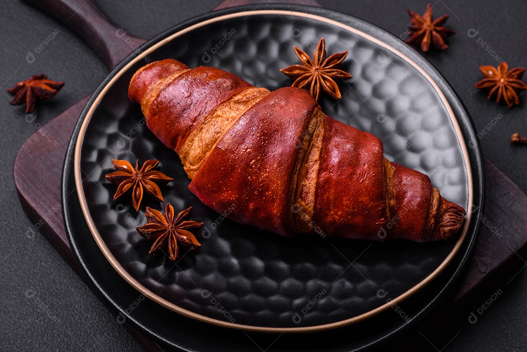Delicioso croissant crocante com chocolate em uma placa de cerâmica preta sobre um fundo escuro de concreto
