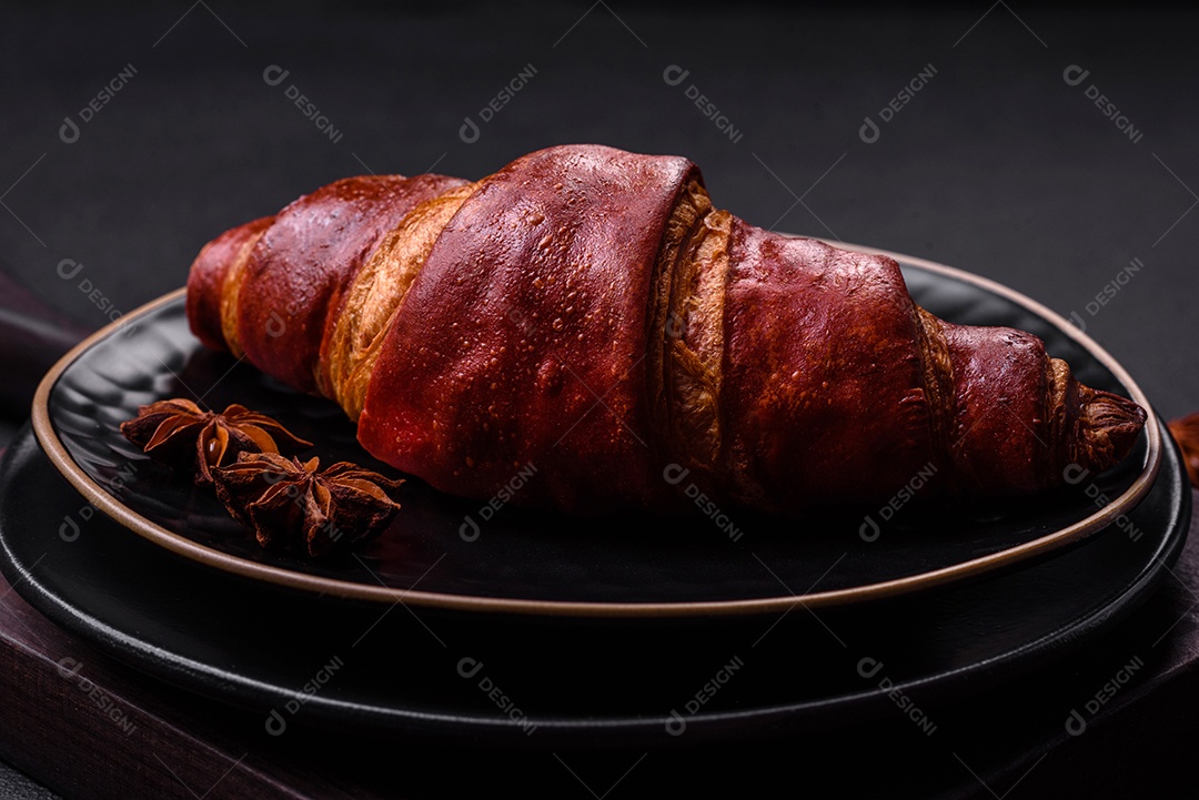 Delicioso croissant crocante com chocolate em uma placa de cerâmica preta sobre um fundo escuro de concreto