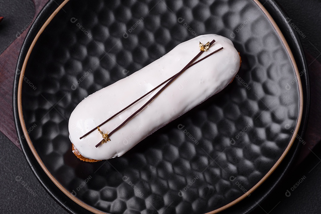 Delicioso profiterole fresco ou éclair com chocolate em uma placa de cerâmica preta sobre um fundo escuro de concreto