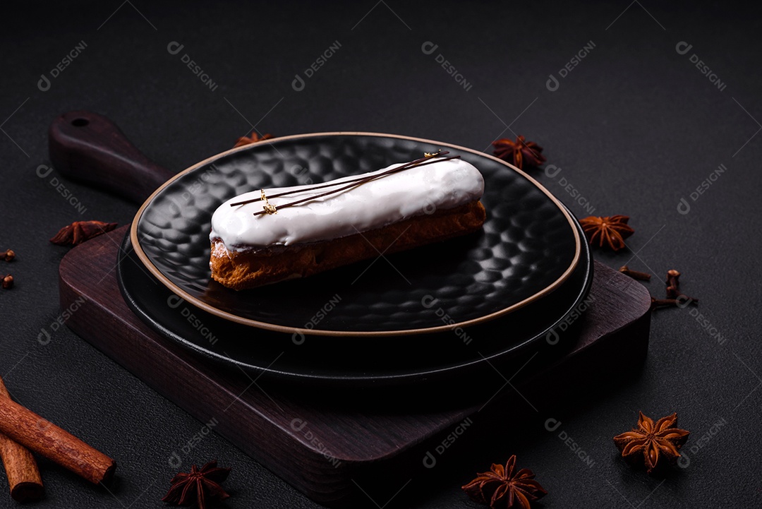Delicioso profiterole fresco ou éclair com chocolate em uma placa de cerâmica preta sobre um fundo escuro de concreto