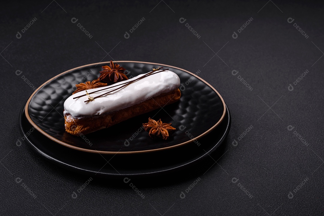 Delicioso profiterole fresco ou éclair com chocolate em uma placa de cerâmica preta sobre um fundo escuro de concreto