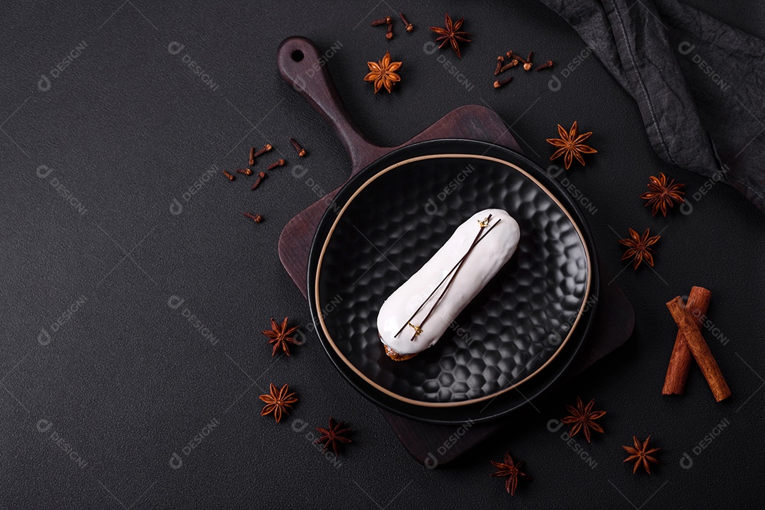 Delicioso profiterole fresco ou éclair com chocolate em uma placa de cerâmica preta sobre um fundo escuro de concreto