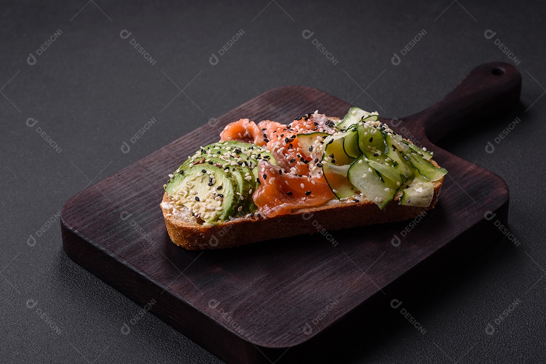 Sanduíche fresco e saboroso com salmão, abacate e sementes de gergelim e linho sobre um fundo escuro de concreto