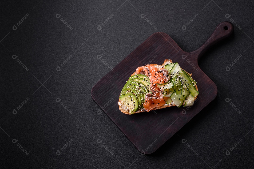Sanduíche fresco e saboroso com salmão, abacate e sementes de gergelim e linho sobre um fundo escuro de concreto