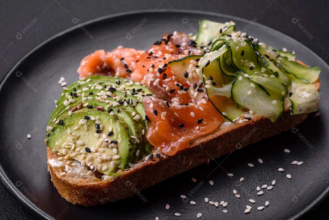 Sanduíche fresco e saboroso com salmão, abacate e sementes de gergelim e linho sobre um fundo escuro de concreto