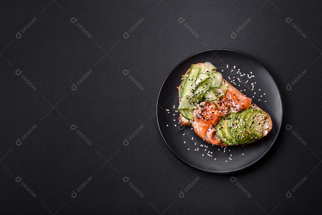 Sanduíche fresco e saboroso com salmão, abacate e sementes de gergelim e linho sobre um fundo escuro de concreto