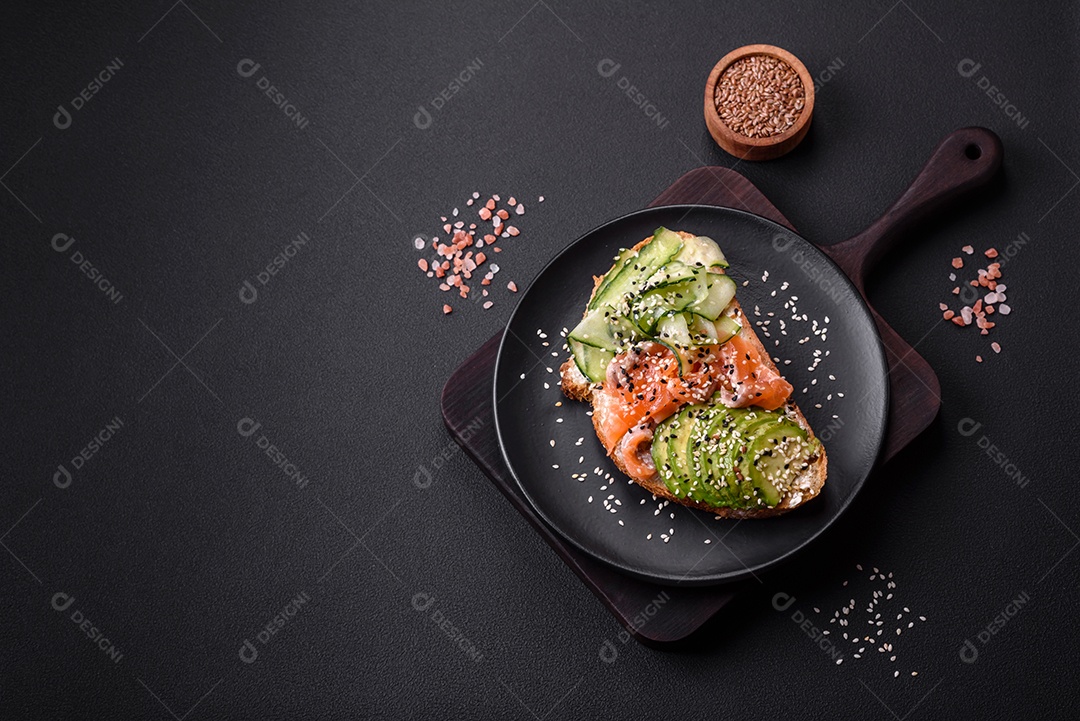 Sanduíche fresco e saboroso com salmão, abacate e sementes de gergelim e linho sobre um fundo escuro de concreto