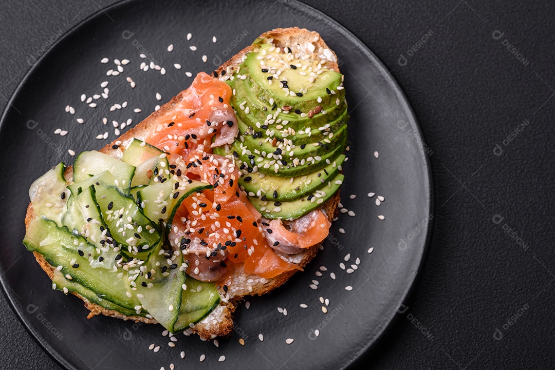 Sanduíche fresco e saboroso com salmão, abacate e sementes de gergelim e linho sobre um fundo escuro de concreto