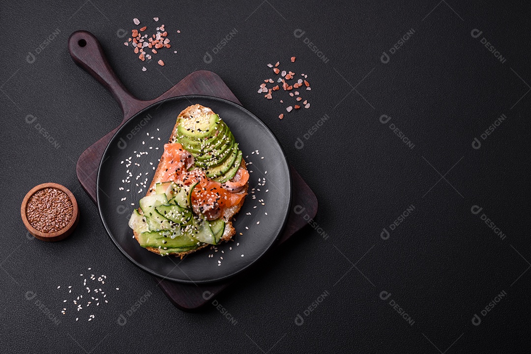 Sanduíche fresco e saboroso com salmão, abacate e sementes de gergelim e linho sobre um fundo escuro de concreto