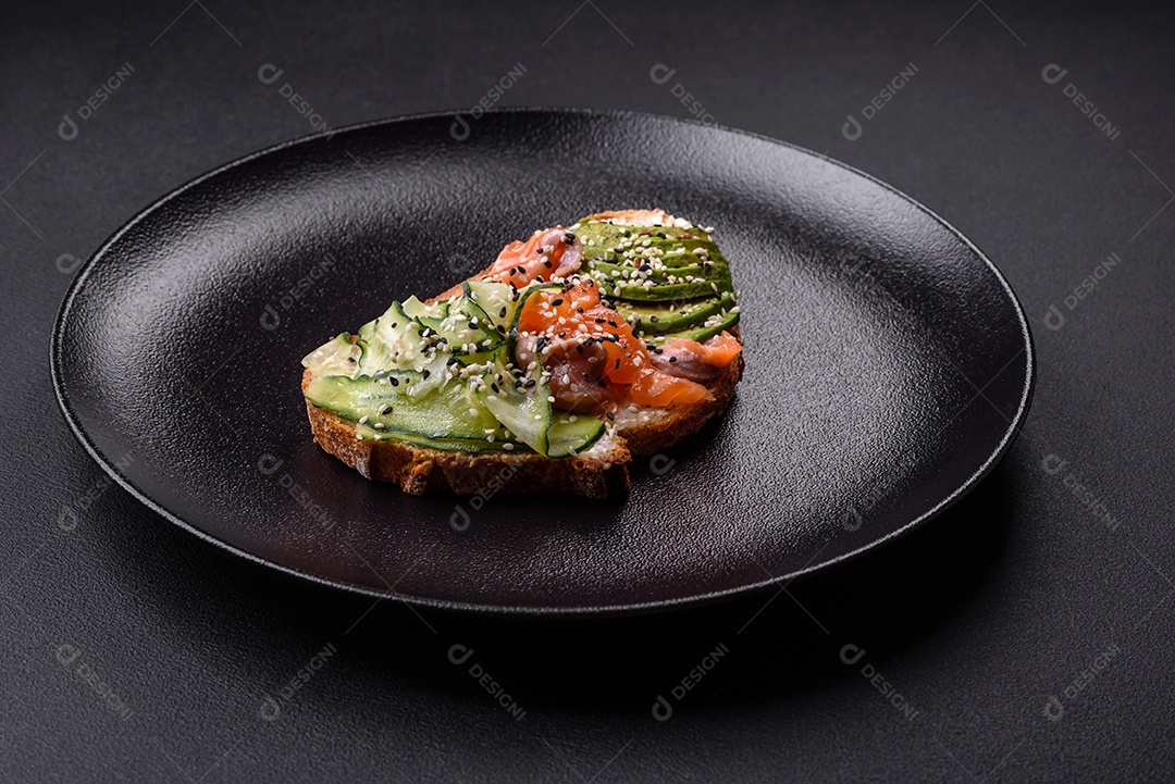 Sanduíche fresco e saboroso com salmão, abacate e sementes de gergelim e linho sobre um fundo escuro de concreto