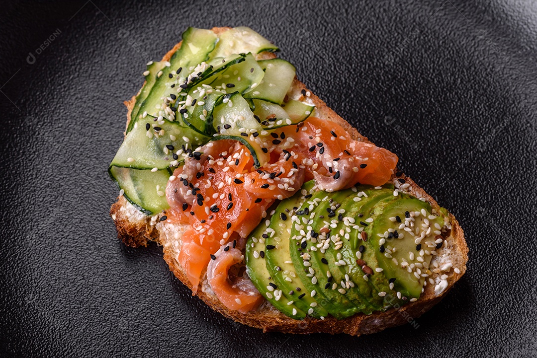Sanduíche fresco e saboroso com salmão, abacate e sementes de gergelim e linho sobre um fundo escuro de concreto