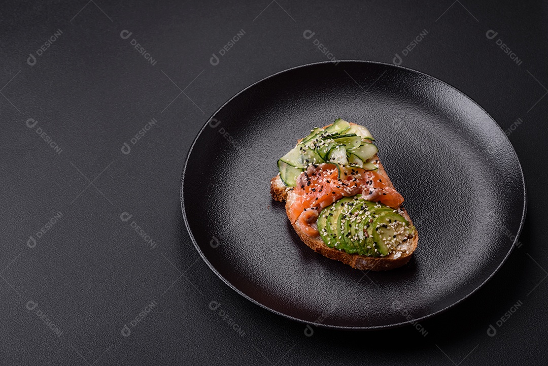 Sanduíche fresco e saboroso com salmão, abacate e sementes de gergelim e linho sobre um fundo escuro de concreto