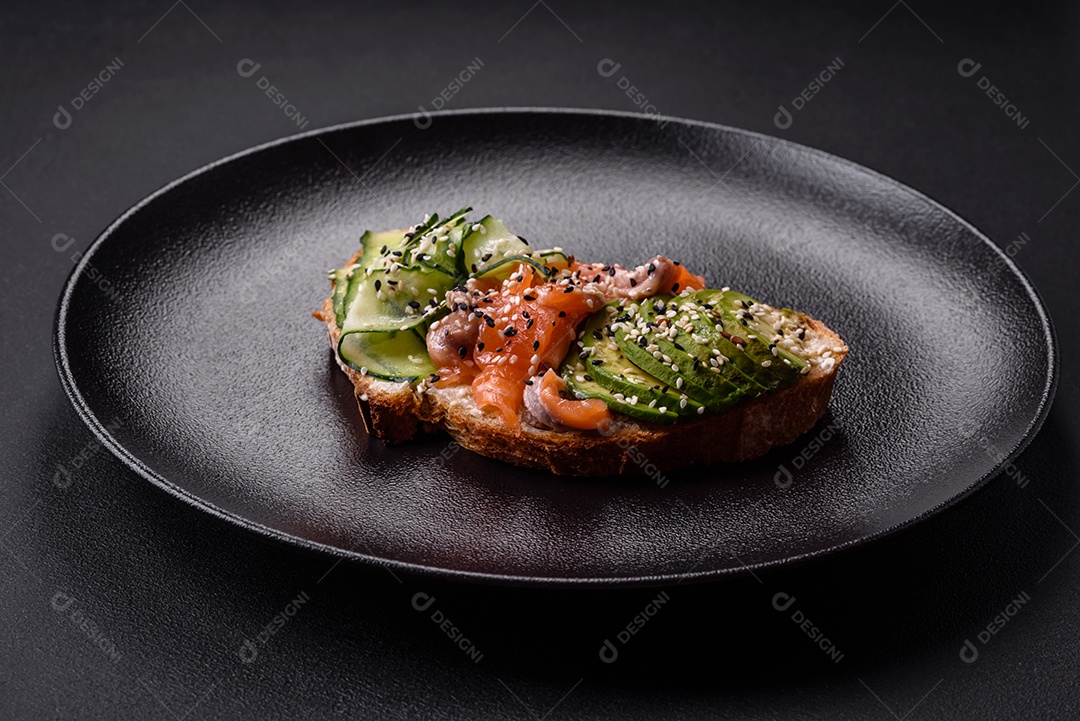 Sanduíche fresco e saboroso com salmão, abacate e sementes de gergelim e linho sobre um fundo escuro de concreto