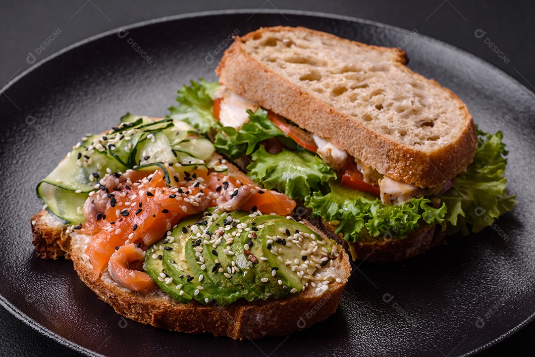Sanduíche fresco e saboroso com salmão, abacate e sementes de gergelim e linho sobre um fundo escuro de concreto
