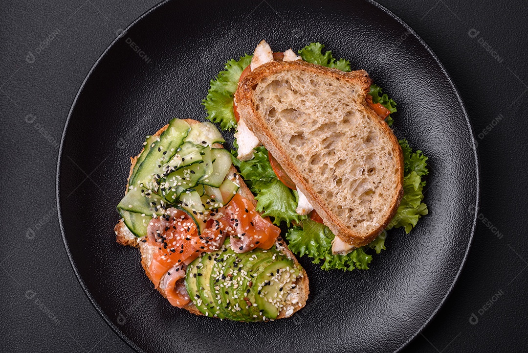 Sanduíche fresco e saboroso com salmão, abacate e sementes de gergelim e linho sobre um fundo escuro de concreto