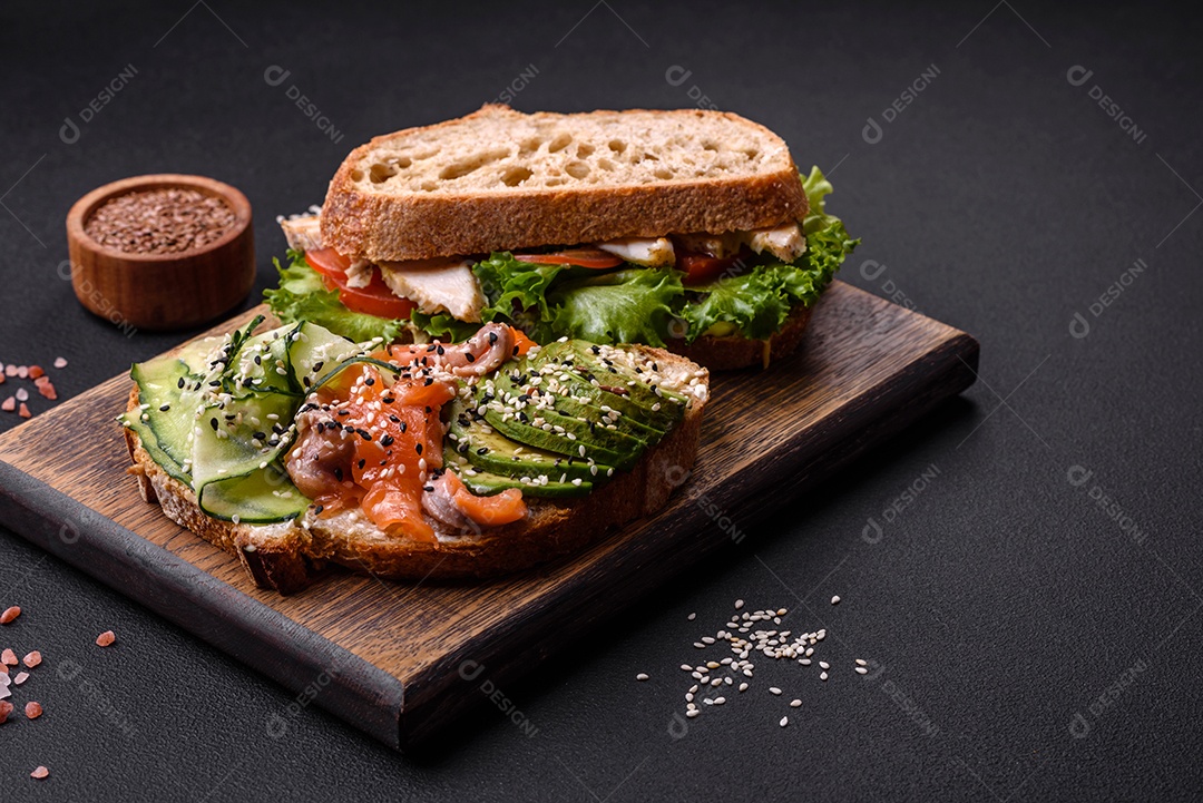 Sanduíche fresco e saboroso com salmão, abacate e sementes de gergelim e linho sobre um fundo escuro de concreto