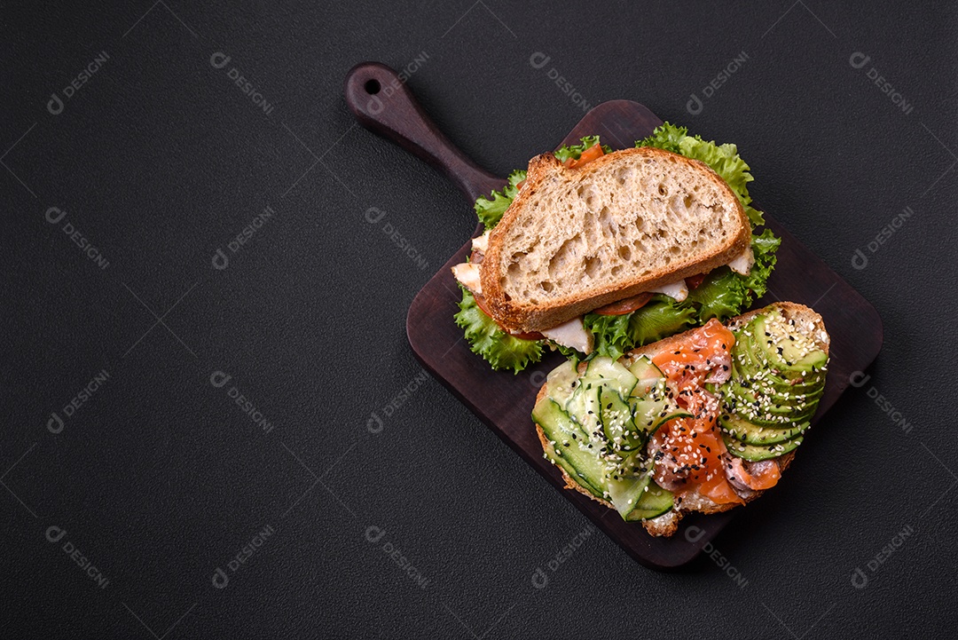 Sanduíche fresco e saboroso com salmão, abacate e sementes de gergelim e linho sobre um fundo escuro de concreto